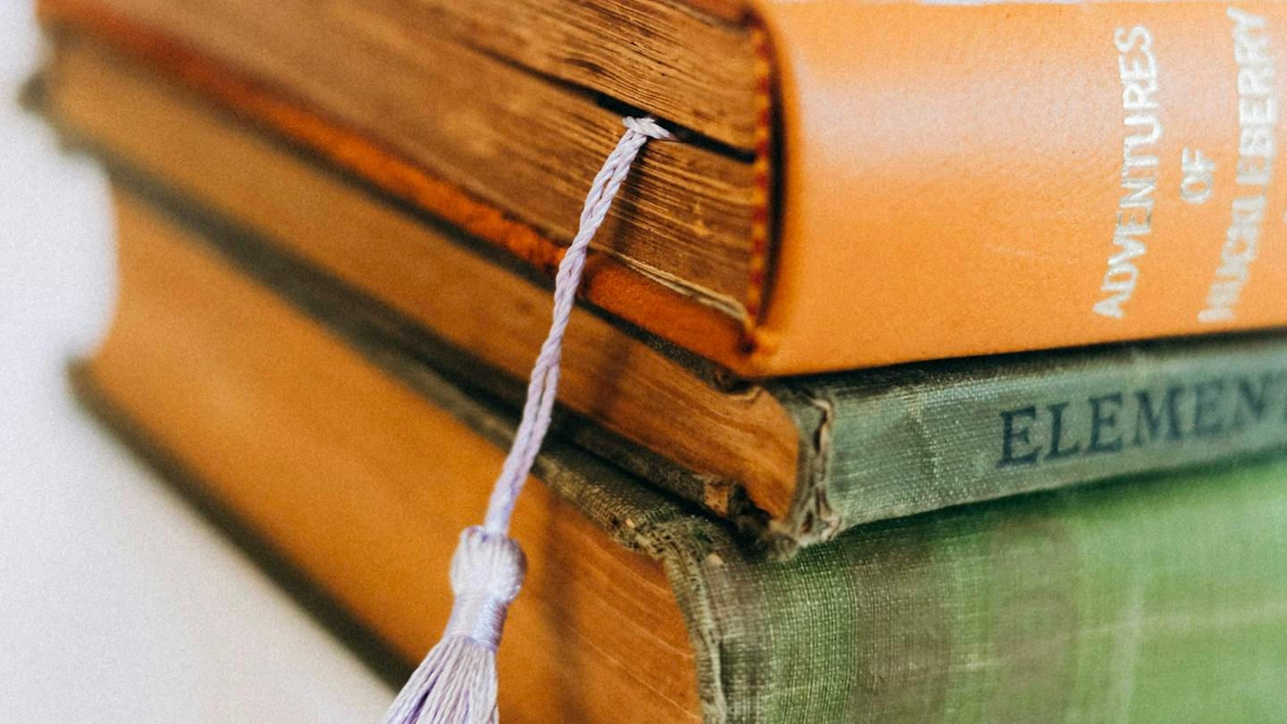 Two old books stacked on each other, a pale purple tassel bookmark tucked between the pages of the top one and hanging over the spine