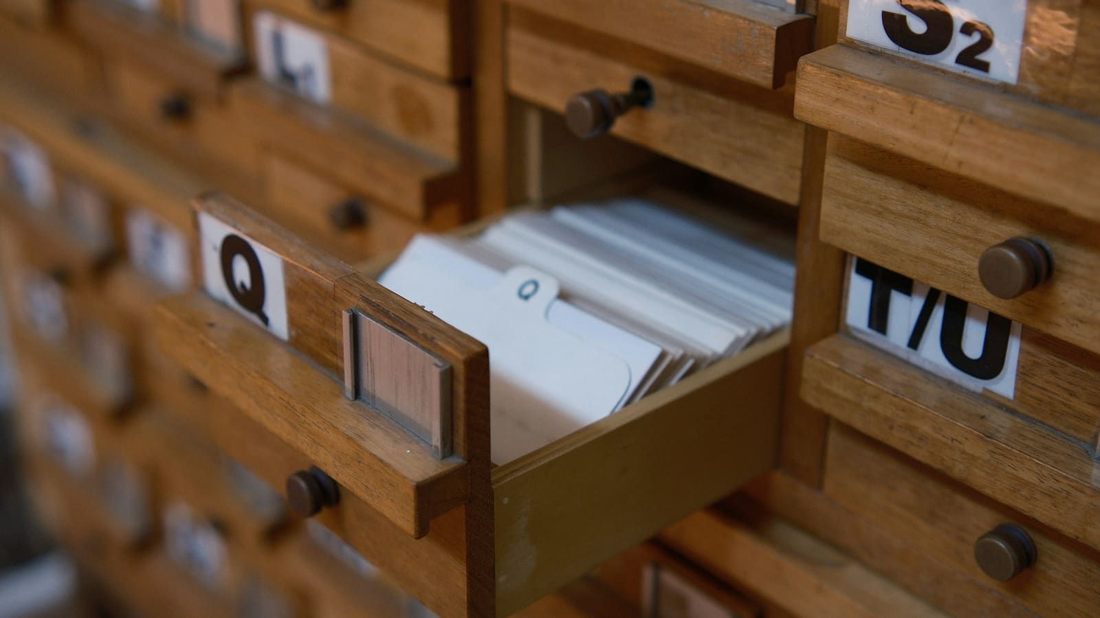 A wall of wooden card-catalogue drawers, one pulled open to show a stack of index cards